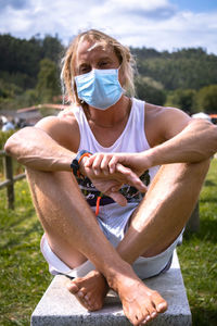 Portrait of man in mask sitting on rock on field