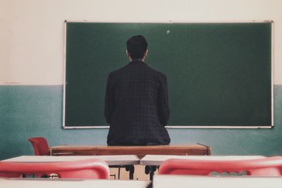 Rear view of man sitting on table looking at blackboard