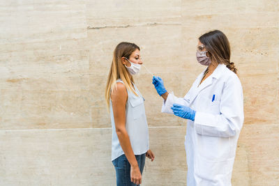 Side view of doctor examining woman while standing by wall outdoors