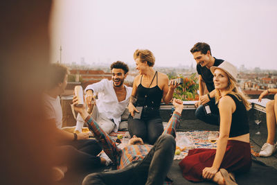 Happy woman playing music on speaker while enjoying with friends at rooftop party