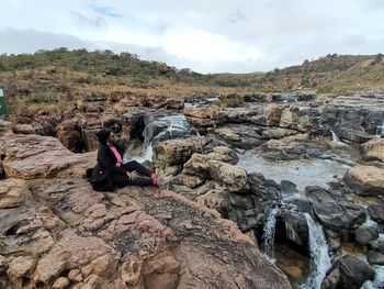 Rear view of woman sitting on rock against sky