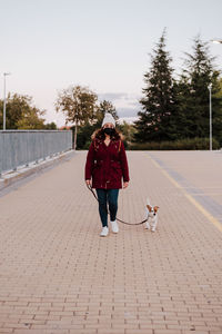 Woman with dog walking on walkway against sky