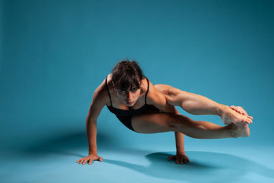 Full length of woman doing yoga against blue background
