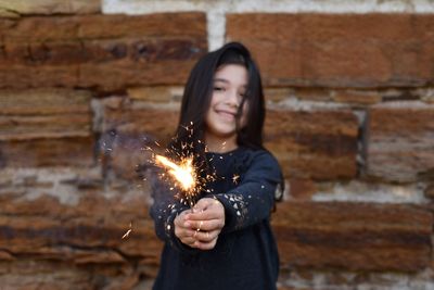 Portrait of girl holding lit sparkler against wall