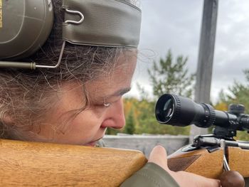 A closeup of a woman aiming with a rifle in the forest on an autumn day.