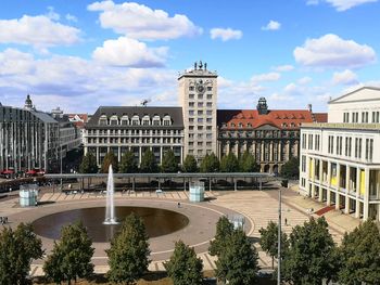 Fountain by buildings in city against sky