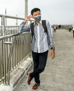 Full length of young man wearing pollution mask standing by railing on bridge 