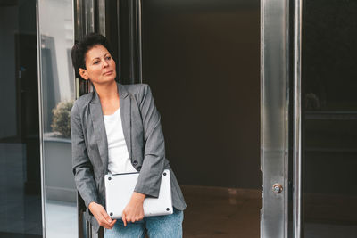 Business woman in jacket and with laptop near door to business center