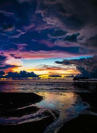 Scenic view of beach against dramatic sky during sunset