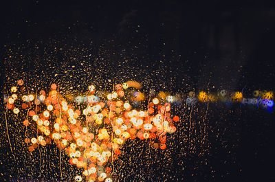 Close-up of wet glass against glowing illuminated lights