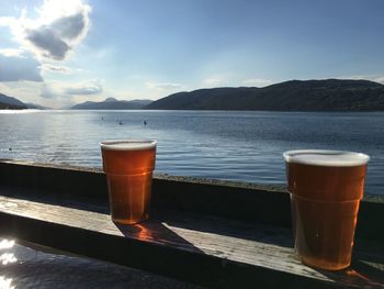 Close-up of beer glasses by railing against lake