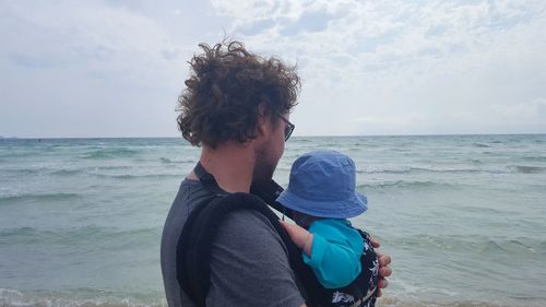 Side view of man and son at beach against sky