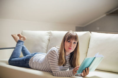 Woman with book while lying on sofa at home
