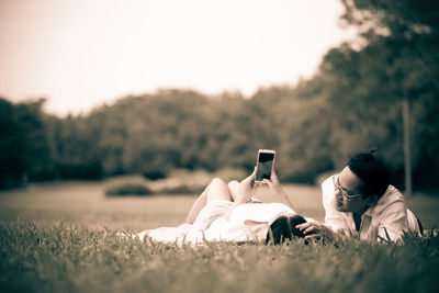 People relaxing on field against sky