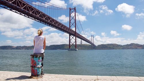 Rear view of woman sitting on bollard against april 25th bridge