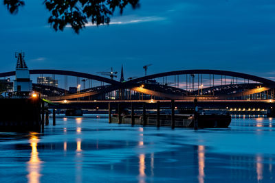 Illuminated bridge over river against sky in city