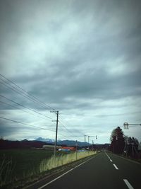 Road passing through field against cloudy sky