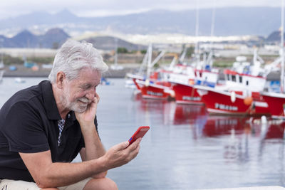 Senior man using smart phone while siting at harbor