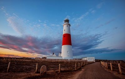 Lighthouse by sea against sky during sunset