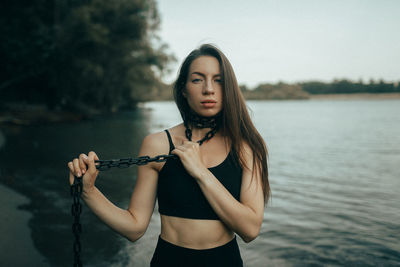 Portrait of young woman standing against lake