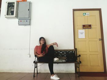 Portrait of woman sitting on bench against classroom