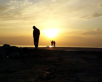 Silhouette men standing on beach against sky during sunset