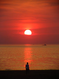 Silhouette woman standing on beach against orange sky