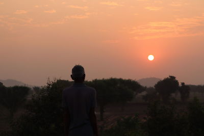 Rear view of silhouette man standing against orange sky