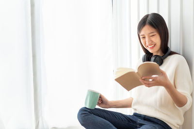 Smiling young woman using mobile phone while sitting at home