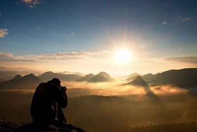 Photographer silhouette above a clouds sea, misty mountains