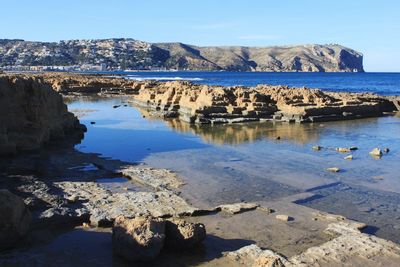 Scenic view of sea and rocks against blue sky