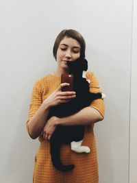 Reflection of young woman holding cat and clicking photograph with smart phone