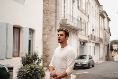 Young man looking away while standing on street in city