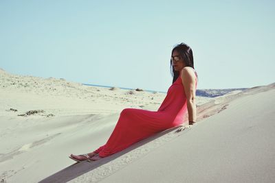 Woman sitting on beach against clear sky