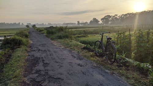 Dirt road amidst field against sky during sunset