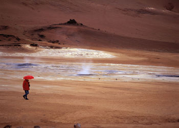 Woman walking with red umbrella at namskard geothermal hot spring area