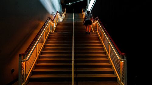 Rear view of woman walking on steps by illuminated railings at night