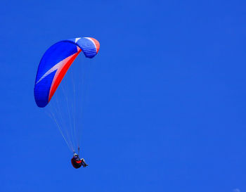Low angle view of person paragliding against clear blue sky 