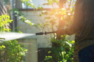 Midsection of man watering plants at backyard