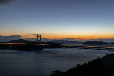 Suspension bridge over river against sky during sunset