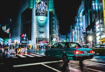 People and cars on street in illuminated city at night