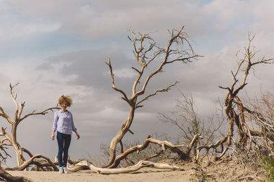 Full length of woman standing on bare tree against sky