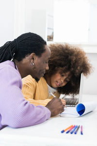 African american dad sitting at table with girl surfing netbook while preparing task for school