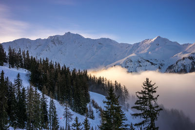 The sun shine down on a cloud filled valley, surrounded by snow covered mountains