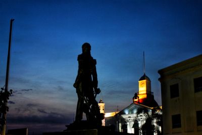 Low angle view of illuminated statue against buildings at dusk