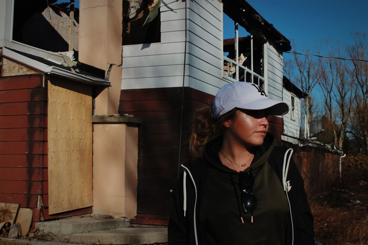 one person, real people, built structure, architecture, building exterior, young adult, clothing, lifestyles, leisure activity, hat, young women, portrait, day, building, front view, standing, waist up, cap, outdoors, hairstyle, contemplation