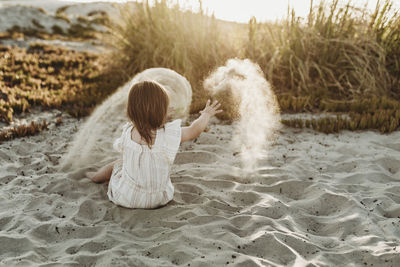 Behind view of young toddler girl throwing sand at sunset