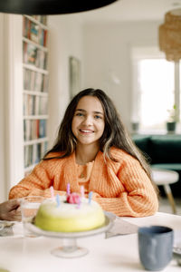 Portrait of happy girl sitting with birthday cake at dining table