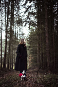 Beautiful young natural woman stands with small dog in the deep woods