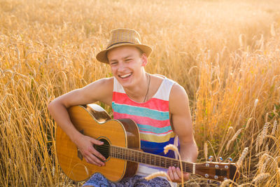 Portrait of a smiling young man playing guitar on field